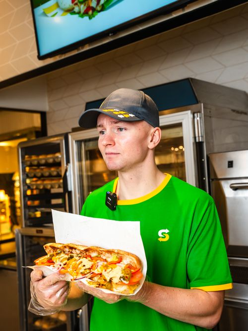 Subway staff member holding a freshly made sandwich
